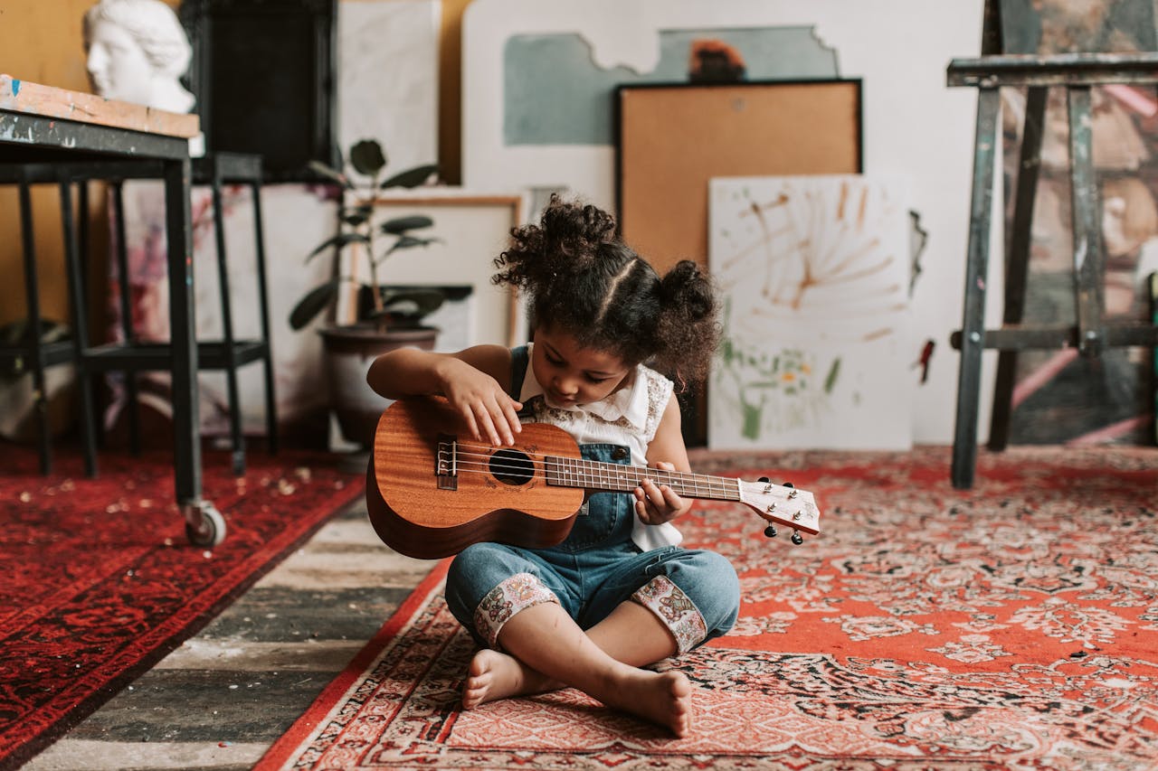 Adorable young girl sitting on the floor playing a ukulele in a vibrant art studio.