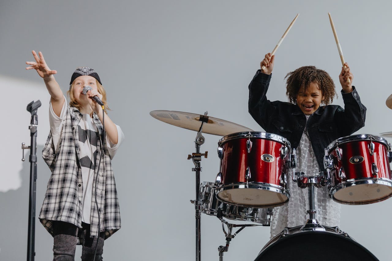 Two children enjoying a lively music performance with drums and microphone.
